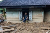 Warga duduk dibekas rumahnya yang tertimbun lumpur akibat banjir bandang di Aceh. Poto: HO